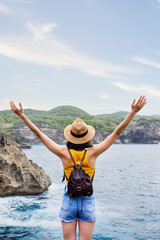 Back view of woman with arms up in Nusa Penida, Bali. Female enjoying freedom in nature.Vertical.Copy space.