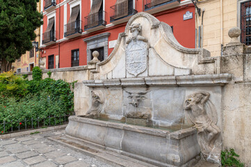 Pilar del Toro in Granada, a beautiful stone fountain surrounded by flowers and with facades of old...