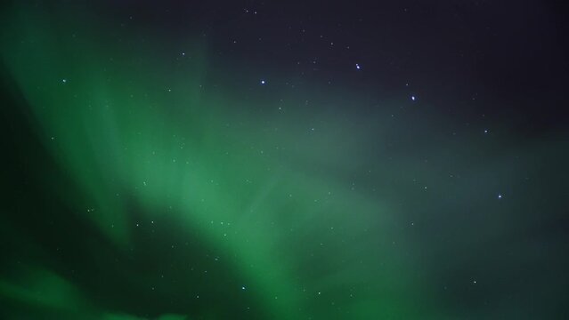 Green and purple Northern Lights (Aurora Borealis) appear overhead on the night sky. Timelapse. 
