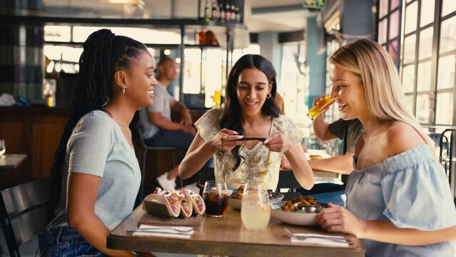 Group of multi-cultural female friends meeting in restaurant taking photo of food on mobile phone and posting to social media - shot in slow motion