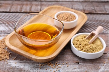 Bowl of natural oil, mustard seeds and powder on wooden table, closeup