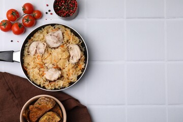 Frying pan with sauerkraut, chicken and products on white tiled table, flat lay. Space for text