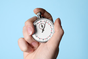 Woman holding vintage timer on light blue background, closeup