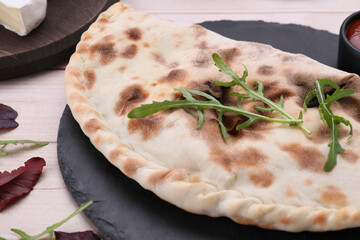 Delicious calzone on light wooden table, closeup
