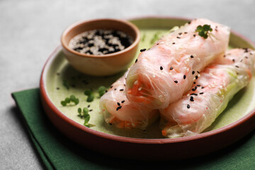 Tasty spring rolls served with soy sauce on grey table, closeup