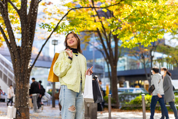 Obraz premium Happy Asian woman holding shopping bag walking and shopping at Shibuya district, Tokyo, Japan in autumn. Attractive girl enjoy outdoor lifestyle travel urban city street on holiday vacation.