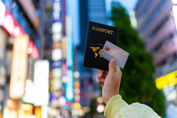 Asian woman hand holding passport and credit card with crowd of people walking and shopping at...