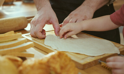 Happy young family enjoying making pie dough or pastries in modern kitchen together, very happy parents teaching little son how to cook bakery at home.