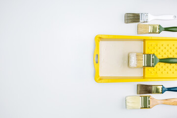  Top view of paint brushes and paint tray on white surface. Interior renovation concept.