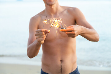 Abstract blur sparklers for celebration. Caucasian man hand holding burning Christmas sparkle on beach