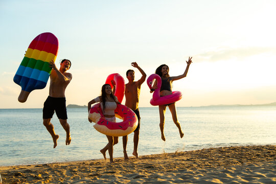 Group of diverse friends having fun swimming and jumping on the tropical summer beach