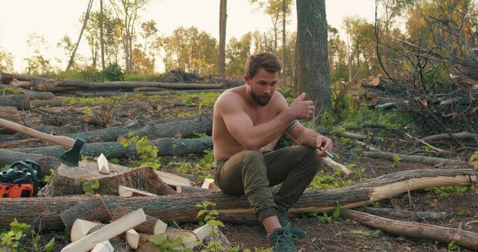 Shirtless tired sweaty man with muscular body smoking cigarettes having rest in the forest, taking break after hard work slow motion tiredness. Smoking break