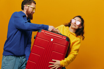 Obraz premium Woman and man smiling, suitcases in hand with yellow and red suitcase smiling merrily and crooked, yellow background, going on a trip, family vacation trip, newlyweds.