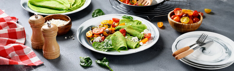 Fresh prepared delicious green spinach crepes served with colorful baked peppers and cherry tomatoes.