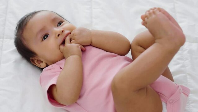 infant baby putting hands in mouth and sucking fingers on a bed