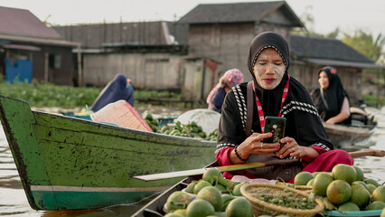 Floating market sellers playing cellphones on the Lok Baintan floating market, South Kalimantan