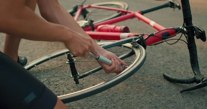 close-up male hands inflate wheel of broken bike with hand pump, vehicle lies on road, punctured wheel problem, health walk outside city, summer sports Close up cropped slow motion