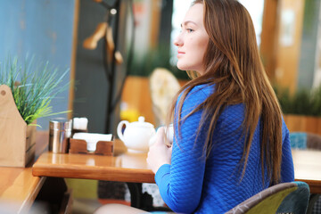 Young girl in cafe sits and drinks tea