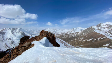 Amazing aerial view of snow covered mountain peaks. Mountain landscape. Blue sky and white clouds. Red rocks. Natural calm background. © chekart