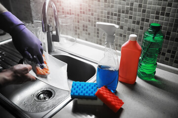 A white bottle with dishwashing gel on the background of a sink with dirty dishes and pouring water from a tap.