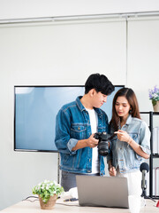 Asian professional photographer man and IT vlogger woman check video file in camera for share on...