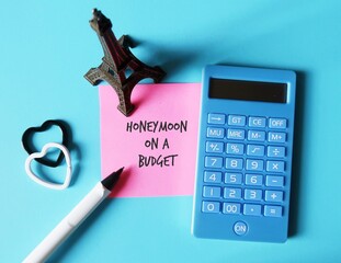 Eiffel model,calculator,pen, hearts on blue background, pink note written HONEYMOON ON A BUDGET,...