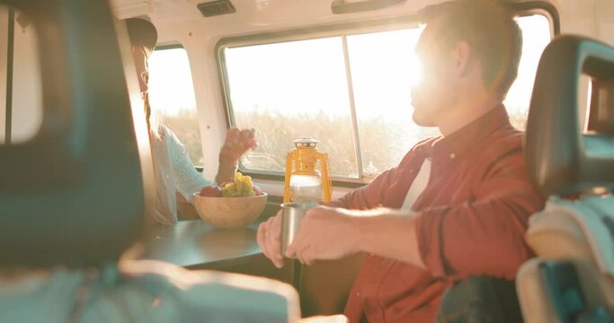 pleasant young couple sitting in camper van, drinking tea, eating fruits, talking in the evening in summer. happy unforgettable moments Relationship Travel Trip Lovely man and woman sit inside of van