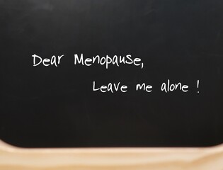 Black chalkboard with blur wood foreground -  text handwritten Dear Menopause, concept of middle aged women dealing or coping with age and menopause symptoms