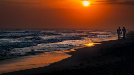 romantic couple holding hands walking along the beach together at sunset