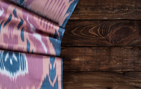Uzbek pink and blue adras textile on wooden background.