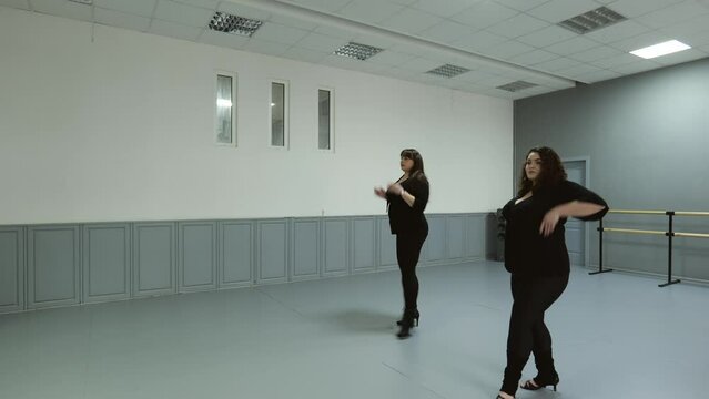 Two fat women in dark clothes are dancing in the hall. Fat women make movements. brunette women