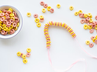 Edible DIY bracelet or necklace for Mothers day. DIY for kids. Bracelet made with froot ring shaped cereal. Making gift with fruit loops for Mothers day. Colored breakfast cereals background.