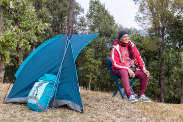 Active Senior Man Camping in Mountains. Sitting in a front of his Tent on Camping Chair.