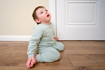 Little baby coughs sitting on the cold laminate floor in the house. Small child is sick and...