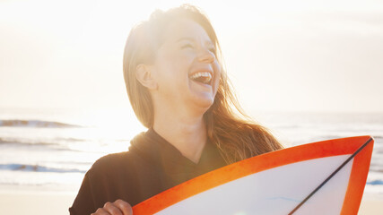 Woman surfer stands with surfing board on the tropical beach and laughs