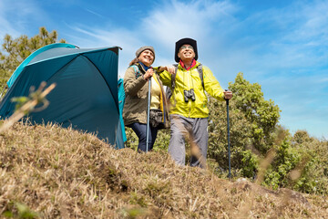 Senior couple of hikers spending a day on a mountain while woman is aiming at distance.