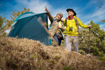 Senior couple of hikers spending a day on a mountain while woman is aiming at distance.