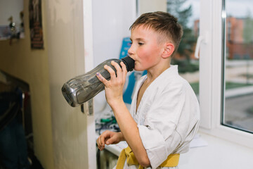 Boy in kemono drinking water after difficult karate sparring