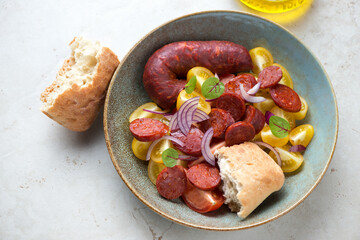 Plate of tomato salad with warm chorizo, red onion and ciabatta, horizontal shot on a light-beige stone background