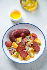 White plate with warm chorizo and tomato salad, vertical shot on a light-grey granite background