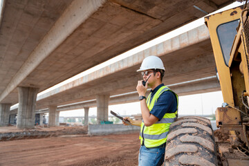 A civil engineer working beside the wheels of grader industrial machine at a road construction site.