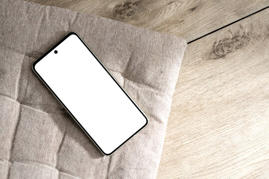 Mobile phone mock up with copy space on neutral beige pillow and wooden desk background, aesthetic summer template with copy space