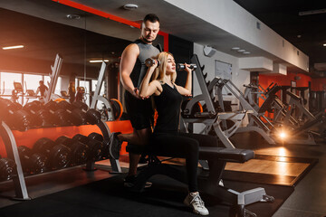 Young couple doing exercises with dumbbells in the gym together. - obrazy, fototapety, plakaty