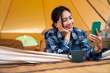 Asian woman drinking coffee with using mobile phone during resting in tent in the morning....