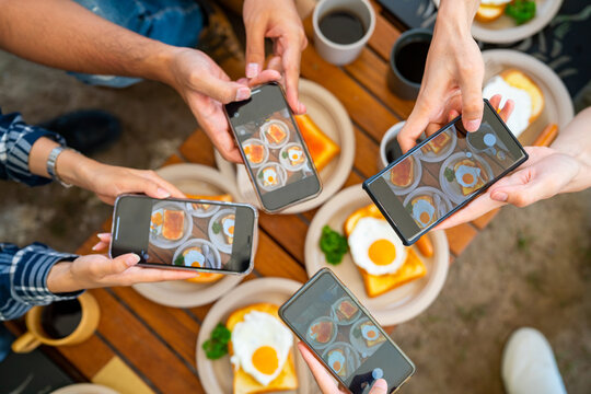 Group of Asian people using mobile phone photography meal during eating breakfast near the tent in the morning. Man and woman enjoy outdoor lifestyle travel nature camping on summer holiday vacation.