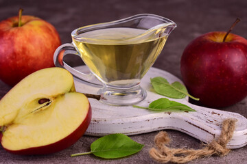 Apple cider vinegar and fresh apple on white wooden board on dark background.
