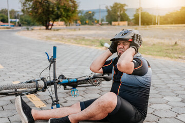 Cyclist on the pavement with a headache. Concept of cyclist suffering with migraine. Male cyclist sitting with headache