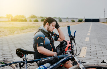 Naklejka premium Male cyclist sitting with headache. Cyclist on the pavement with a headache. Concept of cyclist suffering with migraine