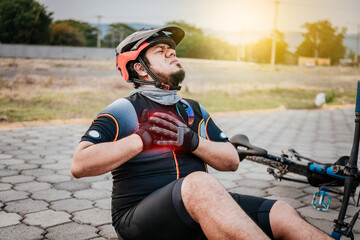 Naklejka premium Cyclist on the pavement with chest pain. Concept of cyclist suffering with hand on his chest. Male cyclist on the ground with heart pain