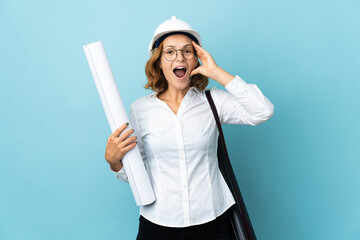 Young architect Georgian woman with helmet and holding blueprints over isolated background with surprise expression